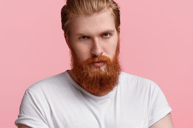 Handsome serious businessman with thick ginger beard, perfect skin, looks directly at camera with mysterious look