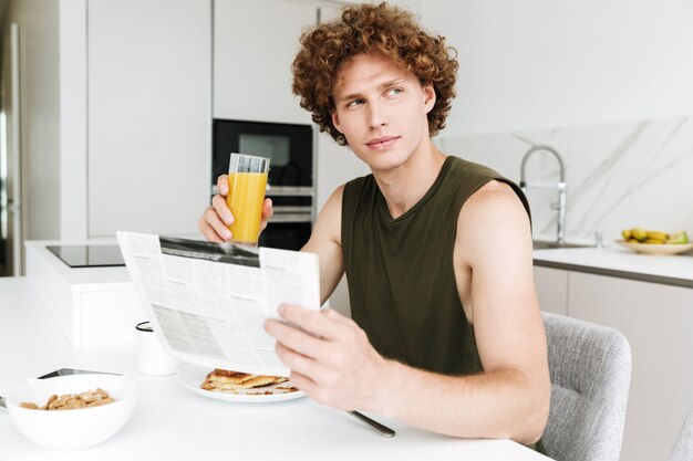 Handsome serious man holding newspaper and drinking juice
