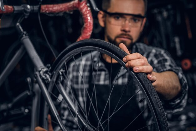 Handsome serious man in protective glasses is fixing bicycle at his own shop.