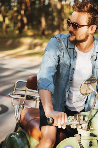 Handsome serious young bearded man sitting on scooter