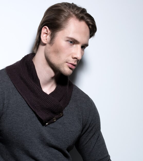 Красивый сексуальный мужчина в сером пуловере позирует над стеной с контрастными тенями и смотрит в сторону.