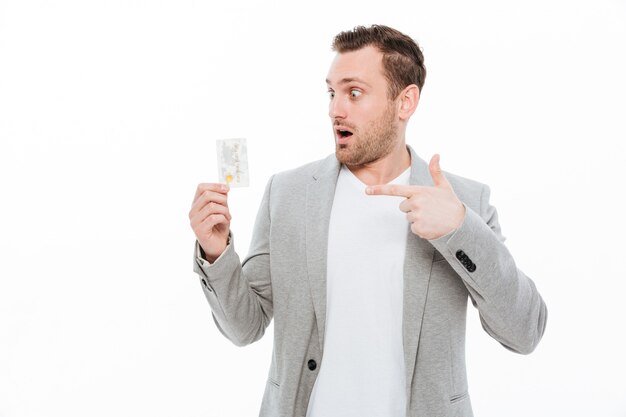 Handsome shocked young businessman pointing while holding credit card.