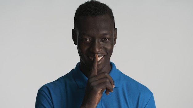 Free photo handsome sly african american guy showing silence gesture on camera and smiling isolated on white background keep secret expression