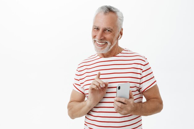 Handsome smiling adult bearded man using wireless earphones and smartphone