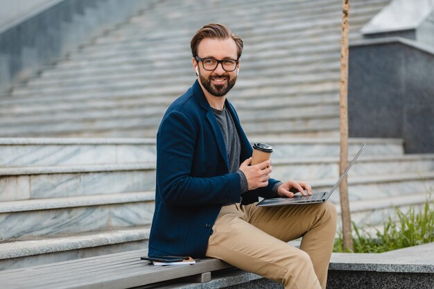 Handsome smiling bearded man in glasses working on laptop