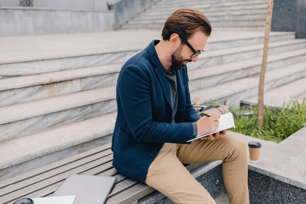 ハンサムな笑顔のひげを生やした男が働いて、ノートブックに書いています