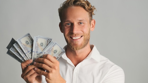 Handsome smiling blond bearded businessman looking happy posing with money on camera isolated on white background