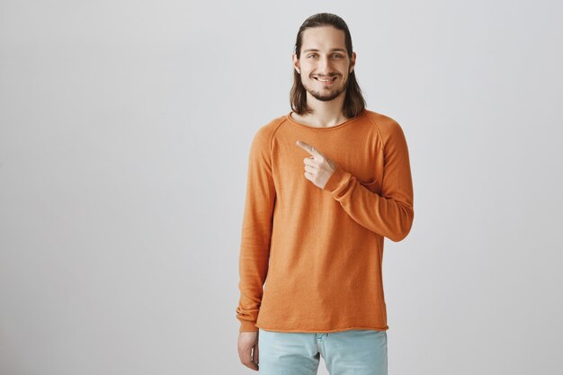 Handsome smiling hipster guy pointing finger left at advertisement