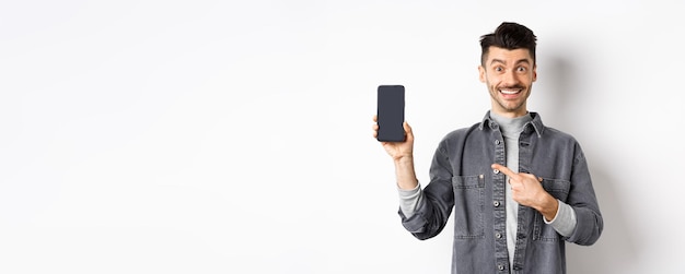 Handsome smiling man pointing finger at smartphone screen showing mobile phone display with happy fa