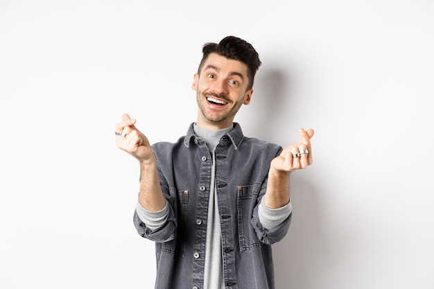 Free photo handsome smiling man showing hand hearts and looking with love at camera, standing on white background