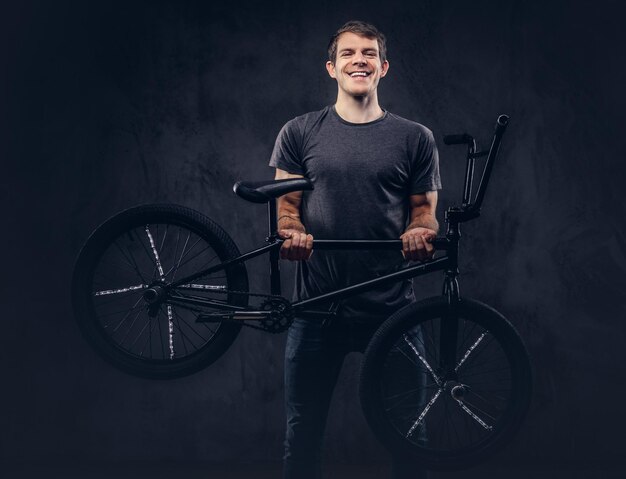 Красивый улыбающийся мужчина в футболке и джинсах держит BMX. Изолированные на темном фоне.