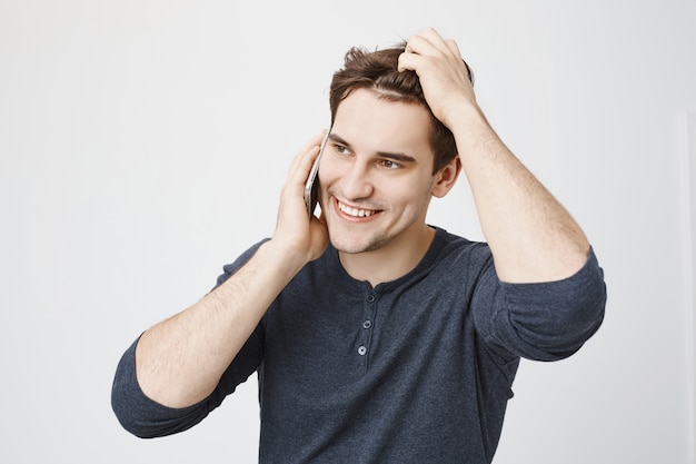 Free photo handsome smiling man talking on phone and run hand through hair