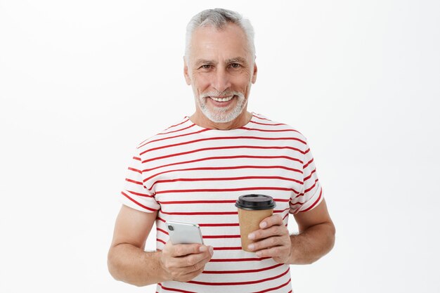 携帯電話を使用してコーヒーとハンサムな笑顔の成熟した男