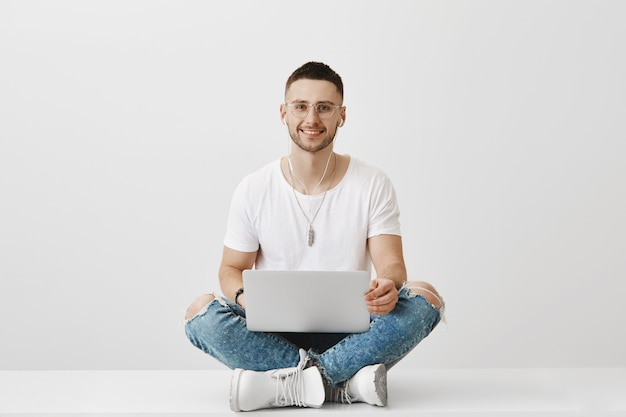 Free photo handsome smiling young guy with glasses posing with his laptop