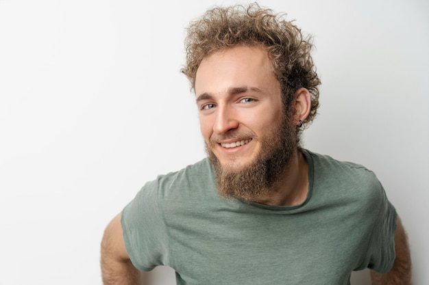 Handsome smiling young handsome bearded wild curly hair man with bright blue eyes isolated on white background Young thinking man in green tshirt on white background