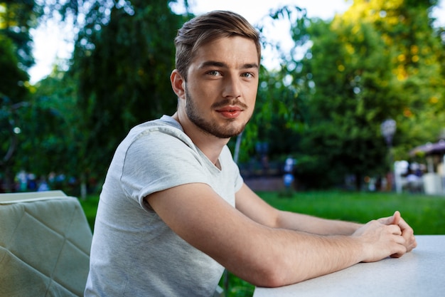 Free photo handsome smiling young man sitting at the table in open-air cafe