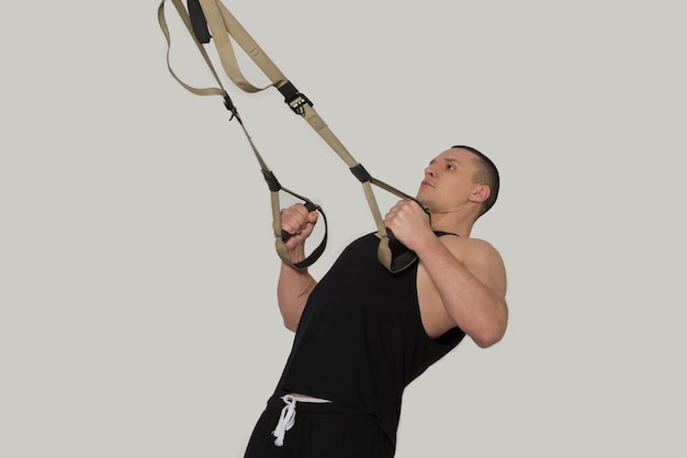 Bello sportivo in uniforme nera che si allena con braccia forti sul bodybuilder trx.