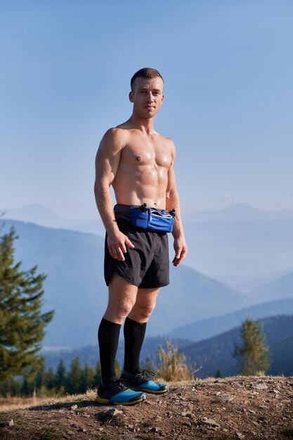 Handsome sports runner standing on top of mountain hill