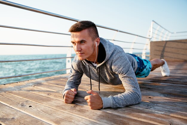 Handsome sportsman in earphones with concentrated face, doing exercises