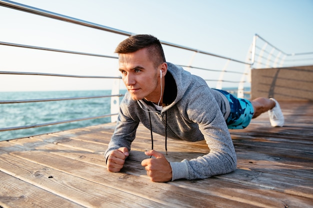 Handsome sportsman in earphones with concentrated face, doing exercises