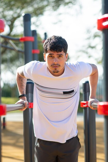 Handsome sportsman working out on sunny day. Man sportive clothes on open air sports ground, exercising using special equipment. Sport, health, working out concept