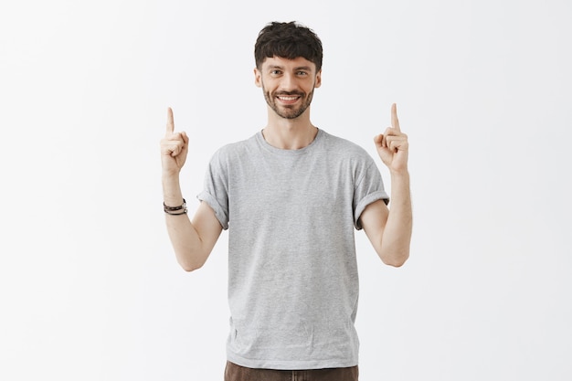 Uomo barbuto elegante bello che indica le dita in alto e sorridendo felice