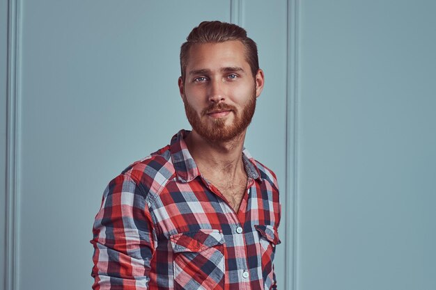 A handsome stylish redhead man in a flannel shirt, posing in a studio against a white wall.