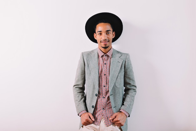 Handsome stylish young man wears black hat checkered shirt and grey jacket on grey