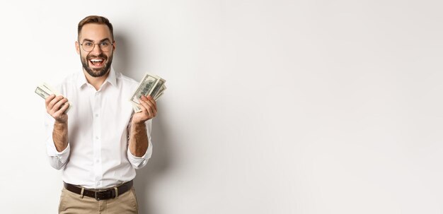 Handsome successful business man counting money rejoicing and smiling standing over white background