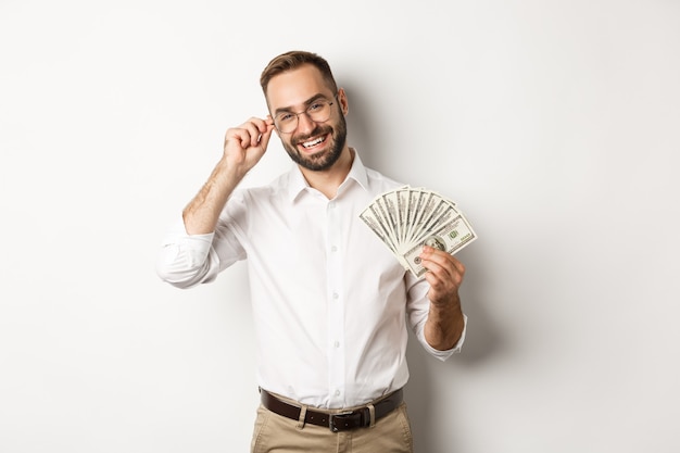 Free photo handsome successful businessman holding money, fixing glasses on nose, standing