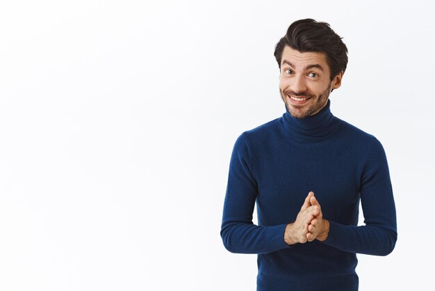 青いハイネックのセーターで手をこすり、喜んで笑顔で取引をもたらすハンサムな成功した男性起業家は、顧客がビジネスパートナーと話している彼の製品を購入することを示唆しています