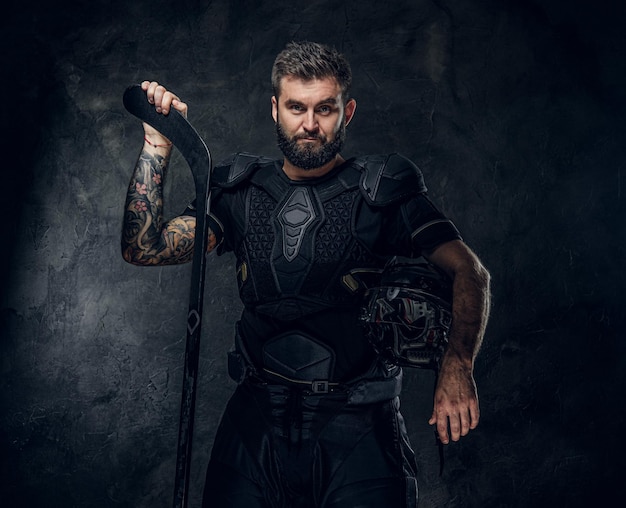 Handsome tattooed hockey player in uniform is posing for photographer.