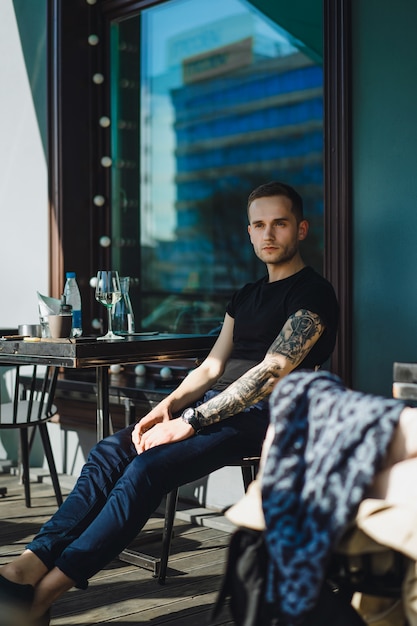 Handsome tattooed man on a summer terrace in a city cafe is drinking wine. street cafe.