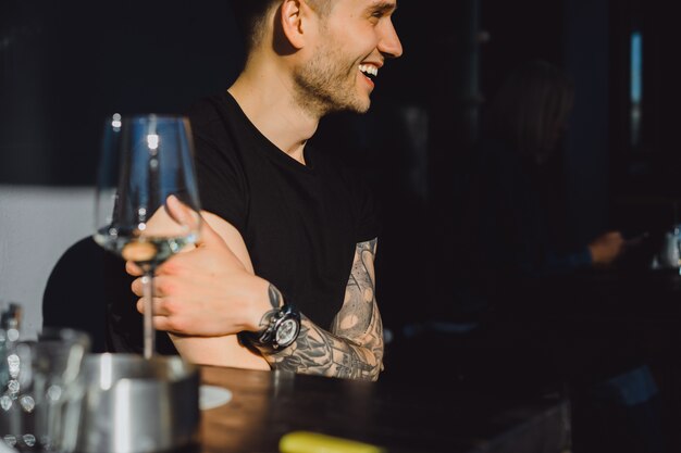 Handsome tattooed man on a summer terrace in a city cafe is drinking wine. Street Cafe.