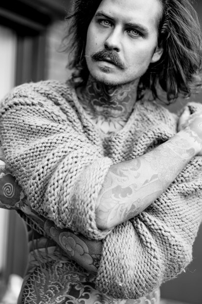 handsome 
tattooed sexy man with long hair and mustache in a knitted sweater. Portrait outside close-up.