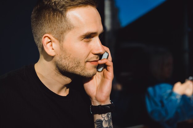 Handsome tattooed young man talking on the phone, close-up portrait, outdoors