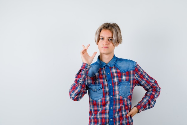 Bel ragazzo adolescente in camicia a quadri che punta all'angolo in alto a sinistra e sembra premuroso, vista frontale.