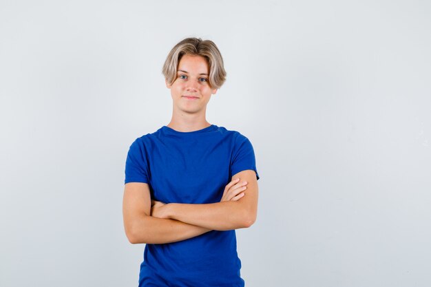 Handsome teen boy keeping arms folded in blue t-shirt and looking cheerful. front view.