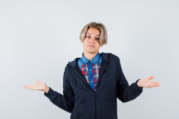 Bel ragazzo adolescente che mostra gesto impotente in camicia, felpa con cappuccio e sembra confuso. vista frontale.