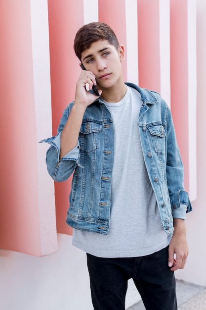 Handsome teenage boy talking on mobile phone standing in front of pink wall