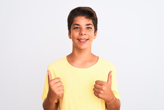 Бесплатное фото Красивый мальчик-подросток, стоящий на белом изолированном фоне, показывает знак успеха, делая позитивный жест с большими пальцами вверх, улыбаясь и счастливый веселое выражение лица и жест победителя