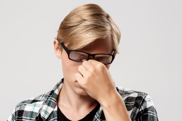  handsome tired blond young man in glasses wearing casual plaid shirt on white wall