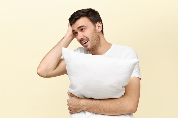 Handsome tired young man holding white pillow