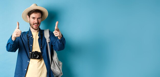 Handsome tourist going on summer vacation with camera and backpack pointing fingers at camera and in