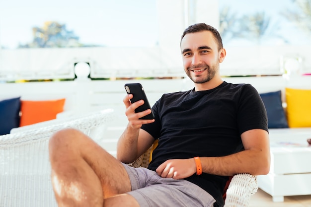 Handsome tourist read and texting sms on mobile phone during relax at sidewalk cafe.