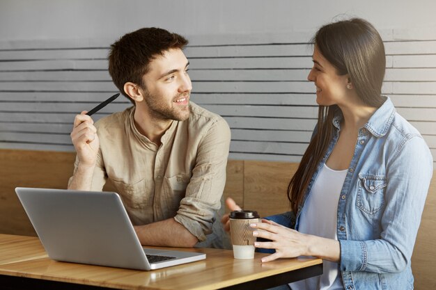 Handsome unshaven male freelancer sitting on a meet in cafe, showing project to customer and talking about work details.