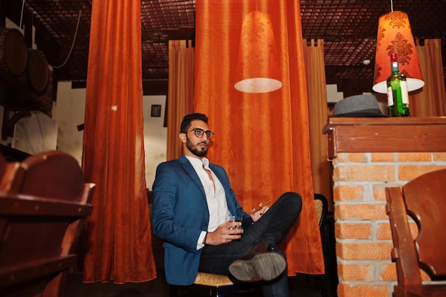 Free photo handsome welldressed arabian man with glass of whiskey and cigar posed at pub