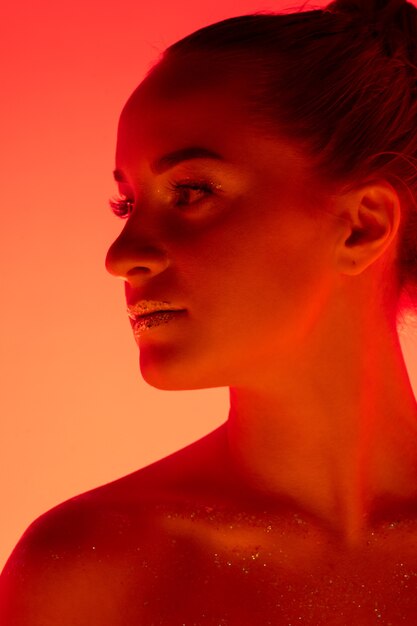 ネオンの光、モノクロで赤オレンジ色のスタジオの背景に分離されたハンサムな女性の肖像画。美しい女性モデル。人間の感情、顔の表情、販売、広告、ファッション、美容の概念。