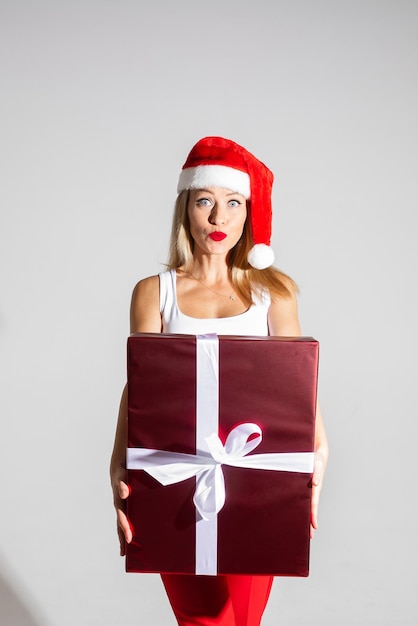 La bella donna con il cappello rosso e bianco di natale tiene un grande regalo