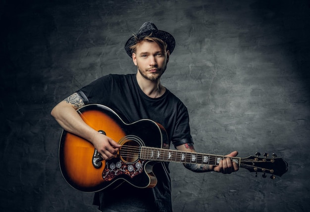 Handsome young acoustic guitar blues player with tattoos on arms performing his musical skills.